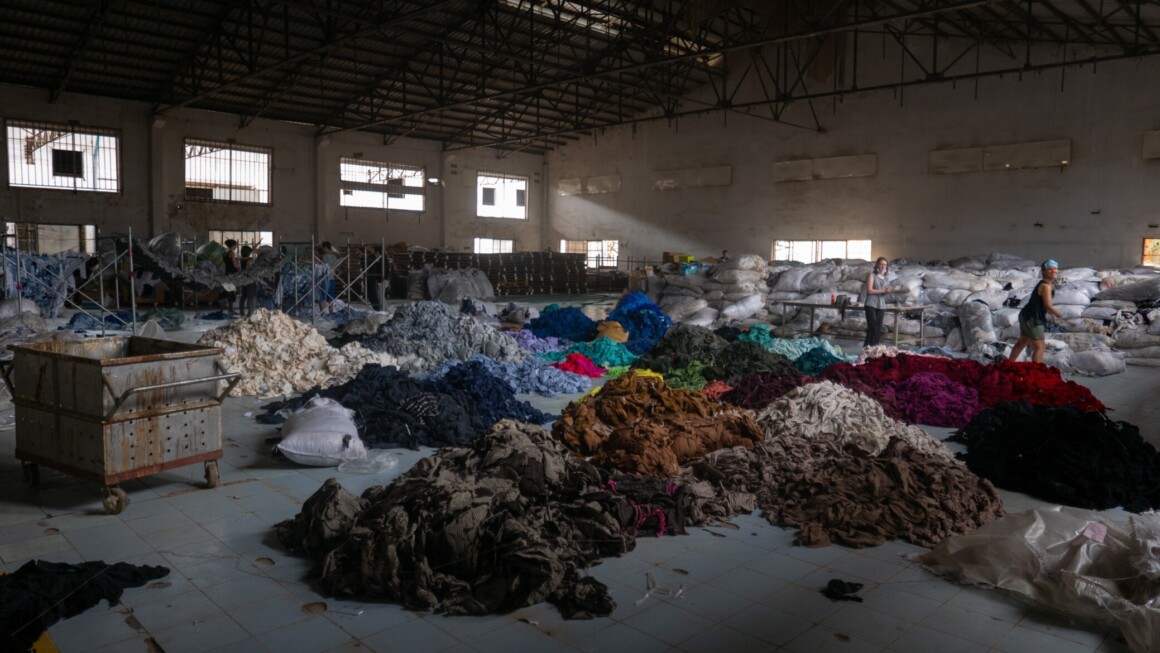 une usine de tri des textiles où on voit des vêtements triés, en piles, par couleurs