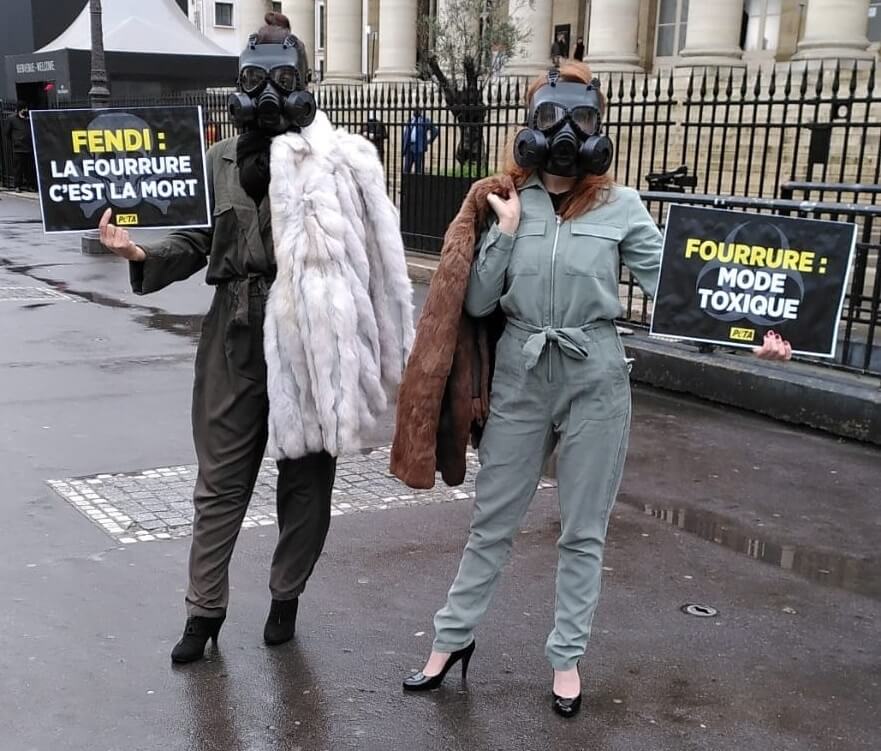 Deux activistes de PETA se tiennent debout devant le Palais de la Bourse à Paris. Elles portent des combinaisons et un masque à gaz. Sur leurs épaules, des manteaux de fourrure. Elles portent dans leurs mains des pancartes "Fendi : la fourrure c'est la mort" et "Fourrure : mode toxique".