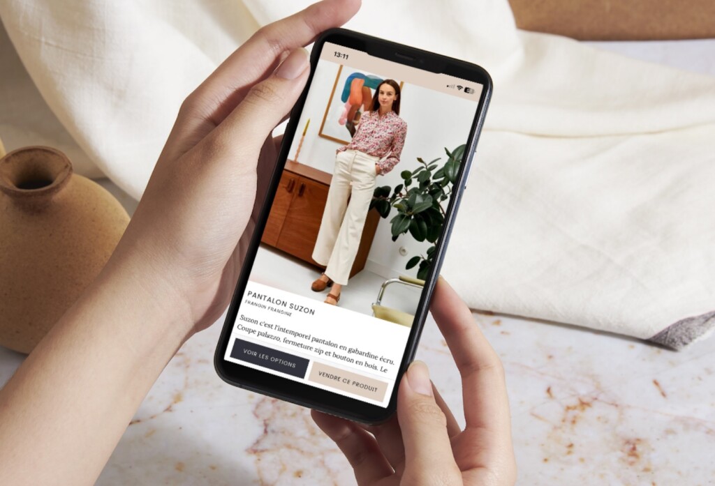 Une personne tient un téléphone entre ses mains. Sur l'écran, l'interface Slöer qui affiche la fiche d'un pantalon.